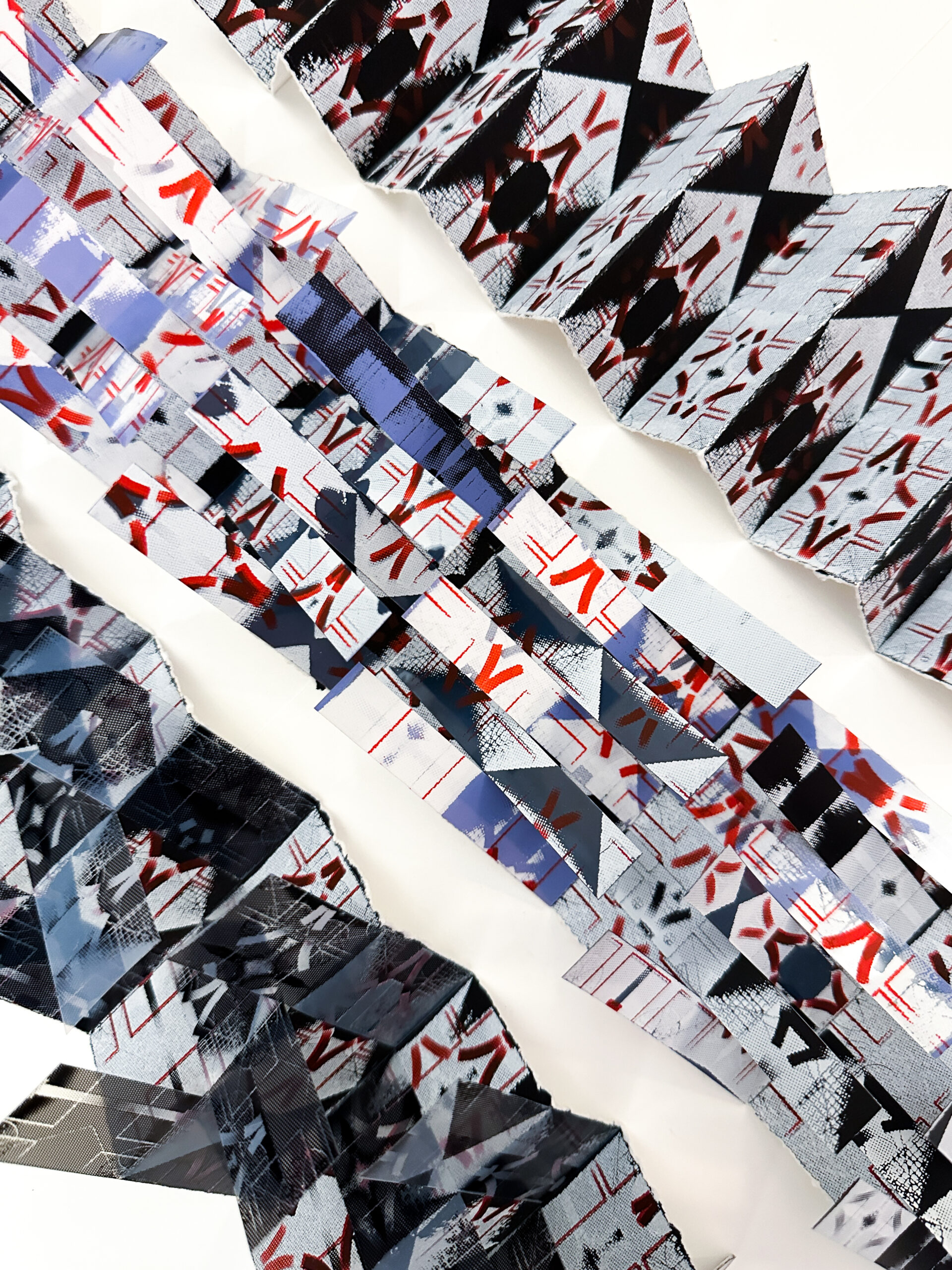 Photo of Jocelyn's artwork on a white background. The artwork consists of strips of paper with patterns in black, red, and blue, and they are folded into accordion-shaped structures. 